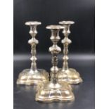 A MATCHED SET OF THREE CONTINENTAL SILVER CANDLESTICKS WITH REMOVABLE DRIP TRAYS, ON SHAPED SQUARE