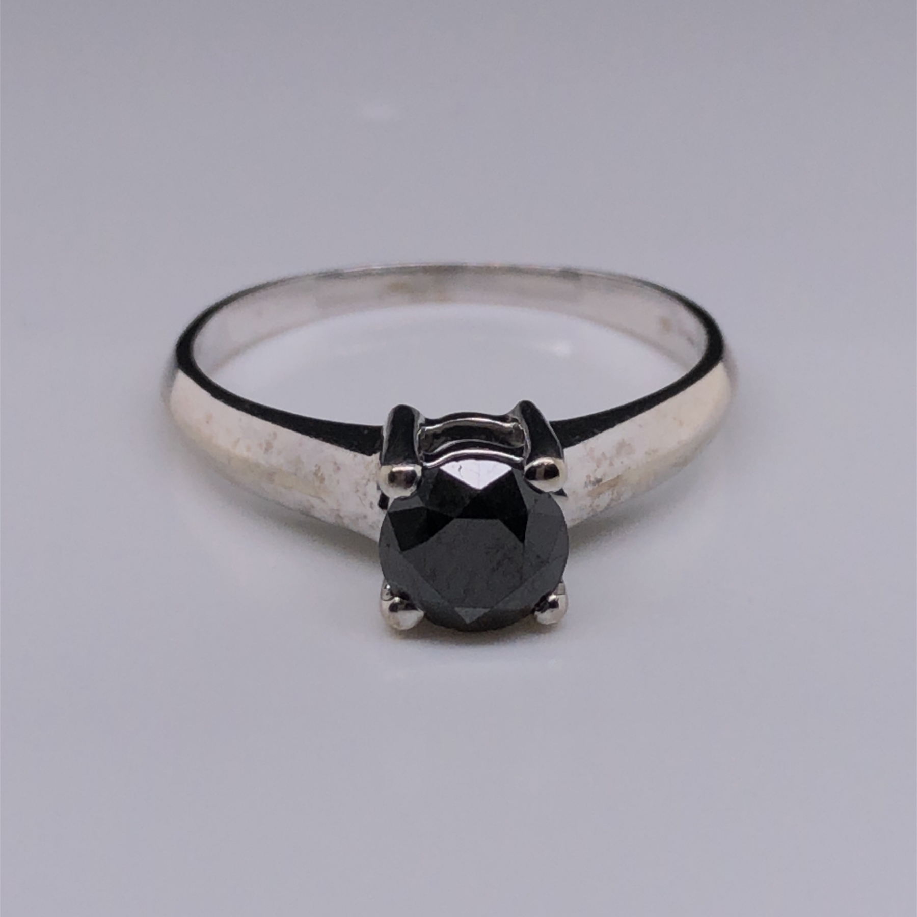 A 9ct WHITE GOLD AND BLACK DIAMOND SOLITAIRE RING. THE ROUND BRILLIANT CUT DIAMOND IN A FOUR CLAW