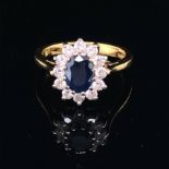 AN 18ct GOLD SAPPHIRE AND DIAMOND CLUSTER RING. THE OVAL CUT CLAW SET SAPPHIRE SURROUNDED BY A