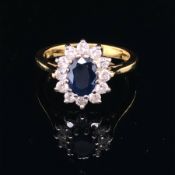 AN 18ct GOLD SAPPHIRE AND DIAMOND CLUSTER RING. THE OVAL CUT CLAW SET SAPPHIRE SURROUNDED BY A