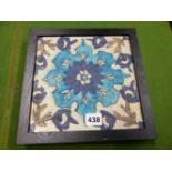 AN IZNIK TILE PAINTED WITH A BLUE STIPPLED FLOWER CENTRAL TO FLOWERING VINES, THE EBONISED FRAME.