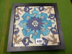 AN IZNIK TILE PAINTED WITH A BLUE STIPPLED FLOWER CENTRAL TO FLOWERING VINES, THE EBONISED FRAME.