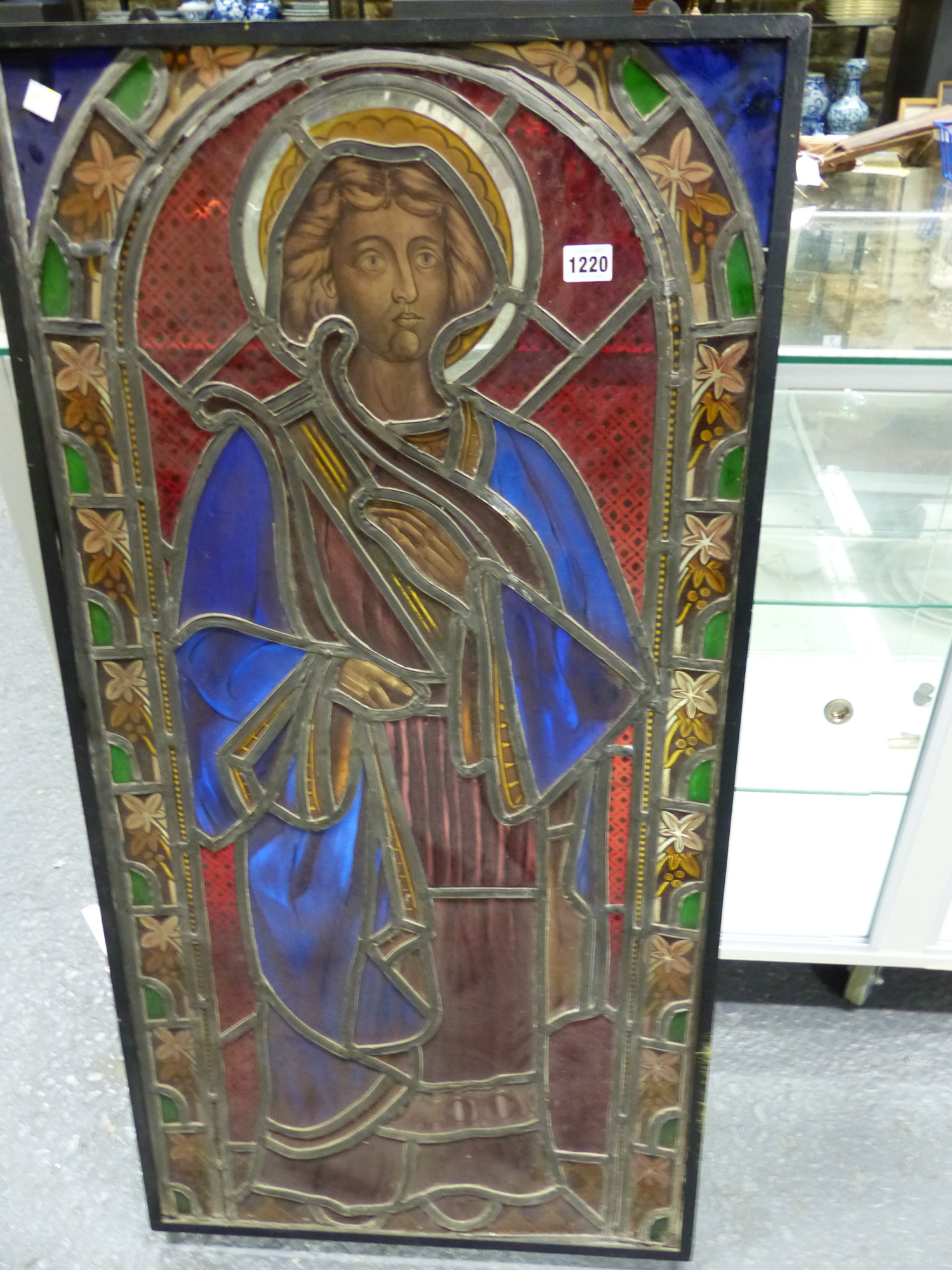 A VICTORIAN STAINED GLASS PANEL OF A SAINT STANDING IN A ROUND ARCHED NICHE, THE LEADED GLASS