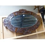 AN OVAL ARTS AND CRAFTS BEVELLED GLASS MIRROR IN A MAHOGANY FRAME CARVED WITH FOUR PANELS OF ENTRE