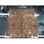 A PAIR OF COPPER PANELS PIERCED AND WORKED WITH FOLIAGE ABOUT HEART SHAPED FRAMED HIRSUTE MASKS.