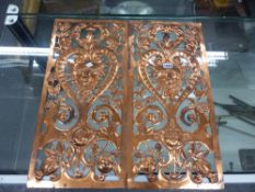 A PAIR OF COPPER PANELS PIERCED AND WORKED WITH FOLIAGE ABOUT HEART SHAPED FRAMED HIRSUTE MASKS.