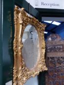 A MIRROR IN GILT FRAME WITH OVAL PLATE, THE SERPENTINE EDGES WITH GESSO FOLIAGE AND ROCAILLE. 93 x