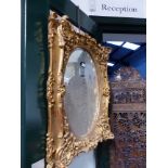 A MIRROR IN GILT FRAME WITH OVAL PLATE, THE SERPENTINE EDGES WITH GESSO FOLIAGE AND ROCAILLE. 93 x