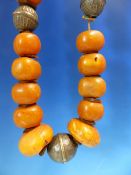 A CONTINUOUS STRING OF IRREGULAR ETHIOPIAN AMBER BEADS INTERSPERSED WITH LOW GRADE SILVER ROUNDELS