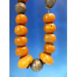 A CONTINUOUS STRING OF IRREGULAR ETHIOPIAN AMBER BEADS INTERSPERSED WITH LOW GRADE SILVER ROUNDELS