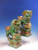 A PAIR OF POTTERY BUDDHIST LIONS GLAZED IN GREEN, OCHRE AND AUBERGINE, THE MALE WITH HIS FOREPAWS ON