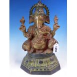 AN INDIAN RED TINTED BRONZE FIGURE OF GANESH HOLDING ATTRIBUTES IN HIS FOUR HANDS AS HE SITS ON A