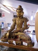 WOODEN CARVING OF A BUDDHA IN TYPICAL POSE, THE WOOD WITH PAINTED GILT DECORATION AND INLAID GLASS