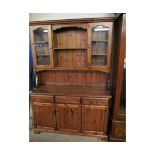 STAINED PINE DRESSER FITTED CENTRALLY WITH TWO SHELVES FLANKED EITHER SIDE WITH GLASS DOORS, THE