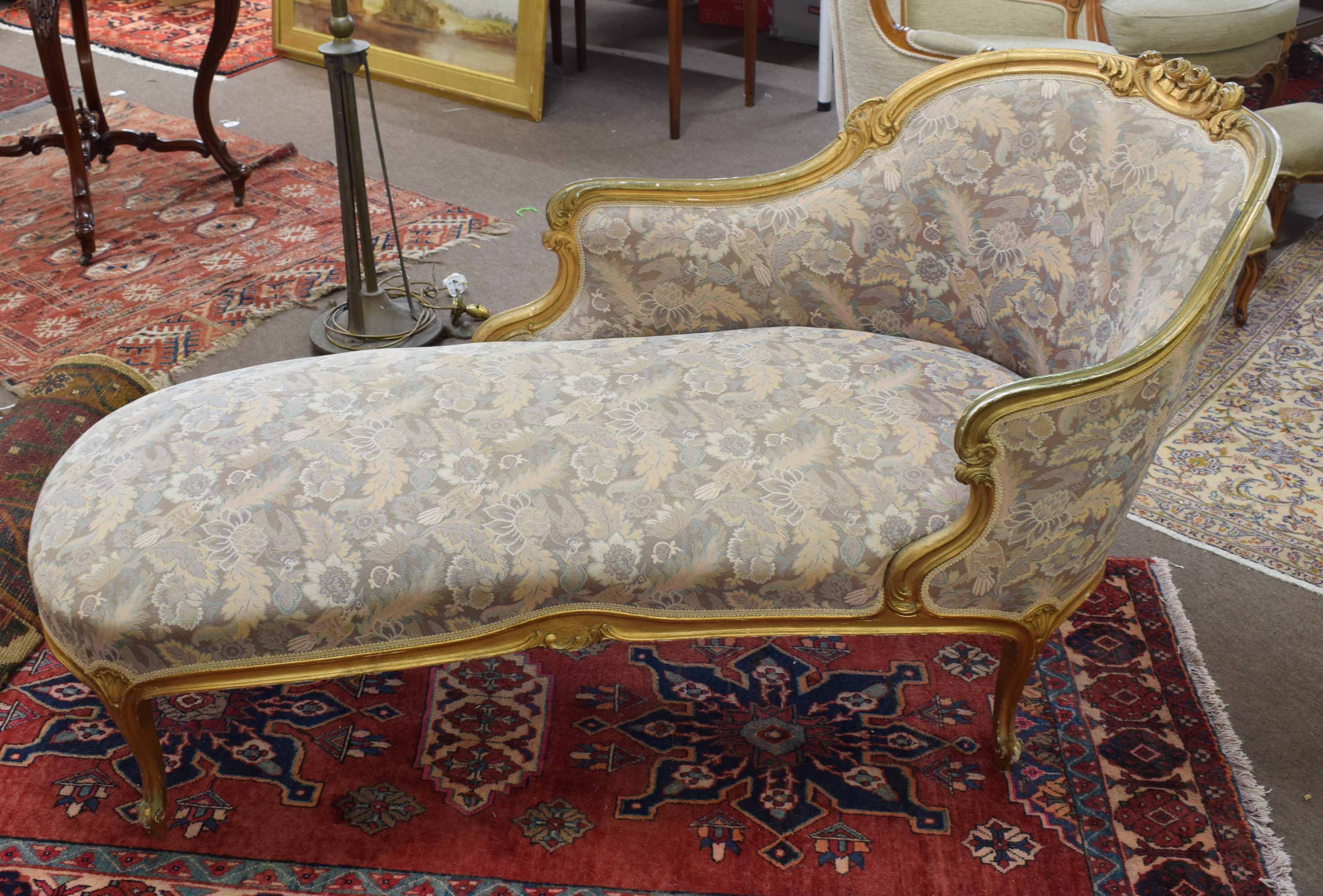 Giltwood chaise longue, swept back encrusted with C-scroll and foliage, upholstered in floral print,