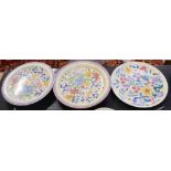 Group of Poole pottery wares, three chargers all with floral designs within pink borders,