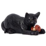 Unusual Bretby pottery model of a cat with glass eyes holding a reel of cotton in its forelegs, 24cm