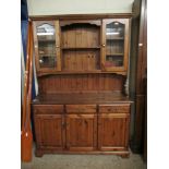 STAINED PINE DRESSER FITTED CENTRALLY WITH TWO SHELVES FLANKED EITHER SIDE WITH GLASS DOORS, THE