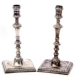 Pair of George II candlesticks with multi-knopped stems to dished square bases with gadrooned edges,