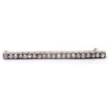 Precious metal diamond set bar brooch, the elongated engraved and pierced bar featuring 21 small old