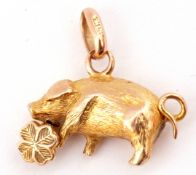 Small yellow metal pig pendant charm holding a four-leaf clover with chased and engraved detail,