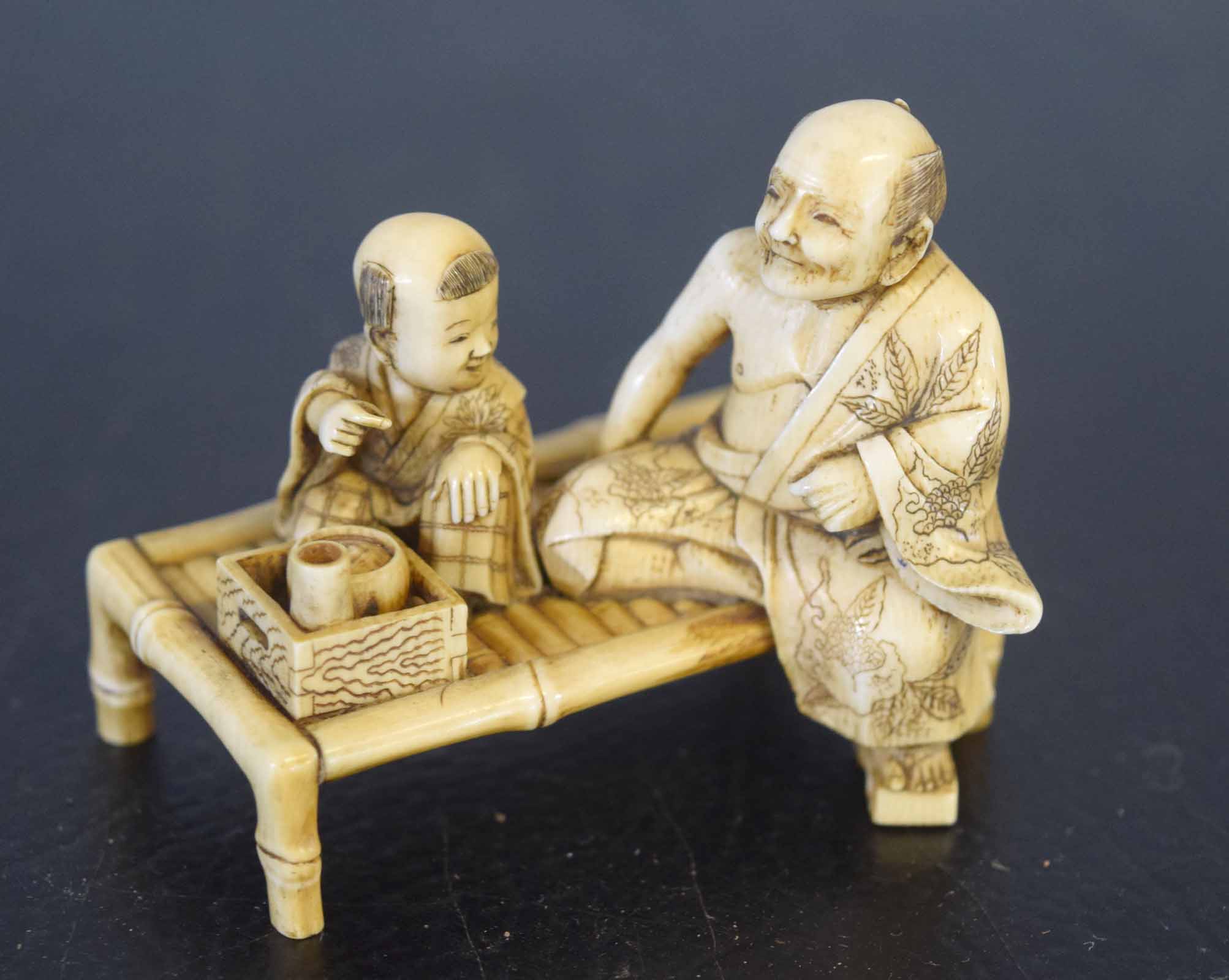 Ivory group of a man and child seated on a table, Meiji period, 6cm long