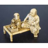 Ivory group of a man and child seated on a table, Meiji period, 6cm long