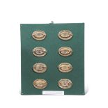 Set of eight embossed brass furniture handles mounted on a baized fronted wooden wall frame, label