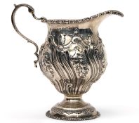 George V cream jug of circular baluster form in George II style, heavily chased and embossed with