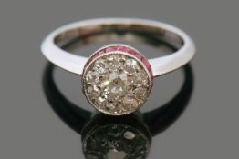 Precious metal diamond and ruby ring, the circular design set with 11 pave set diamonds, the