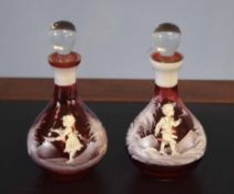 Pair of ruby small carafes and stoppers decorated in white with a Mary Gregory type design, (2)