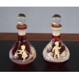 Pair of ruby small carafes and stoppers decorated in white with a Mary Gregory type design, (2)