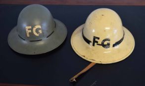 Two vintage firemen's tin hats, each initialled FG, one grey and one beige