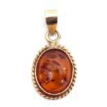 9ct gold and amber pendant, the oval shaped cabochon amber centre within a polished and rope twist