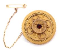 Victorian gold circular target brooch centring a small round garnet in a starburst engraved setting,
