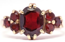 9ct gold garnet cluster ring centring a large faceted oval shaped garnet with 3 small circular