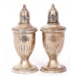 Pair of antique silver loaded peppers of vase form, pierced detachable tops, half fluted bodies,