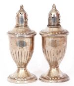 Pair of antique silver loaded peppers of vase form, pierced detachable tops, half fluted bodies,