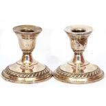 Pair of white metal loaded dwarf candlesticks with urn shaped socles on circular stepped gadrooned