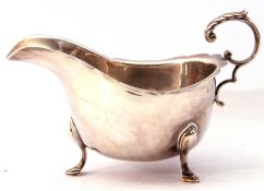 George V silver sauce boat with card cut rim and leaf capped flying scroll handle on cast hoof feet,