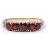 Antique garnet ring, featuring five round faceted garnets raised between carved scroll shoulders