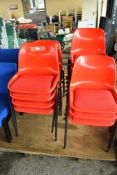FIFTEEN RED METAL FRAMED AND IMPACT MOULDED PLASTIC STACKING CHAIRS