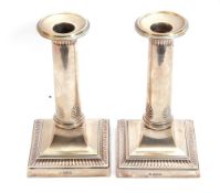 Pair of George V silver candlesticks of plain circular tapering columns, applied with card cut