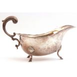 George V silver sauce boat with shaped card cut rim, flying leaf capped scroll handle, standing on