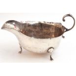George VI silver sauce boat with shaped rim and capped flying scroll handle, on three cast hoof