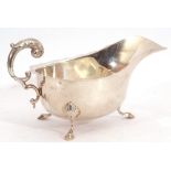 Mid-20th century silver sauce boat with card cut rim and flying scroll capped handle on three hoofed