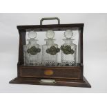 Edwardian oak three-bottle tantalus applied with three plated spirit labels for Brandy, Whisky and