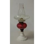 An opaline glass pedestal oil lamp, having cranberry glass font