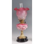 A Victorian brass pedestal oil lamp, having cranberry tinted and acid etched shade over moulded pink