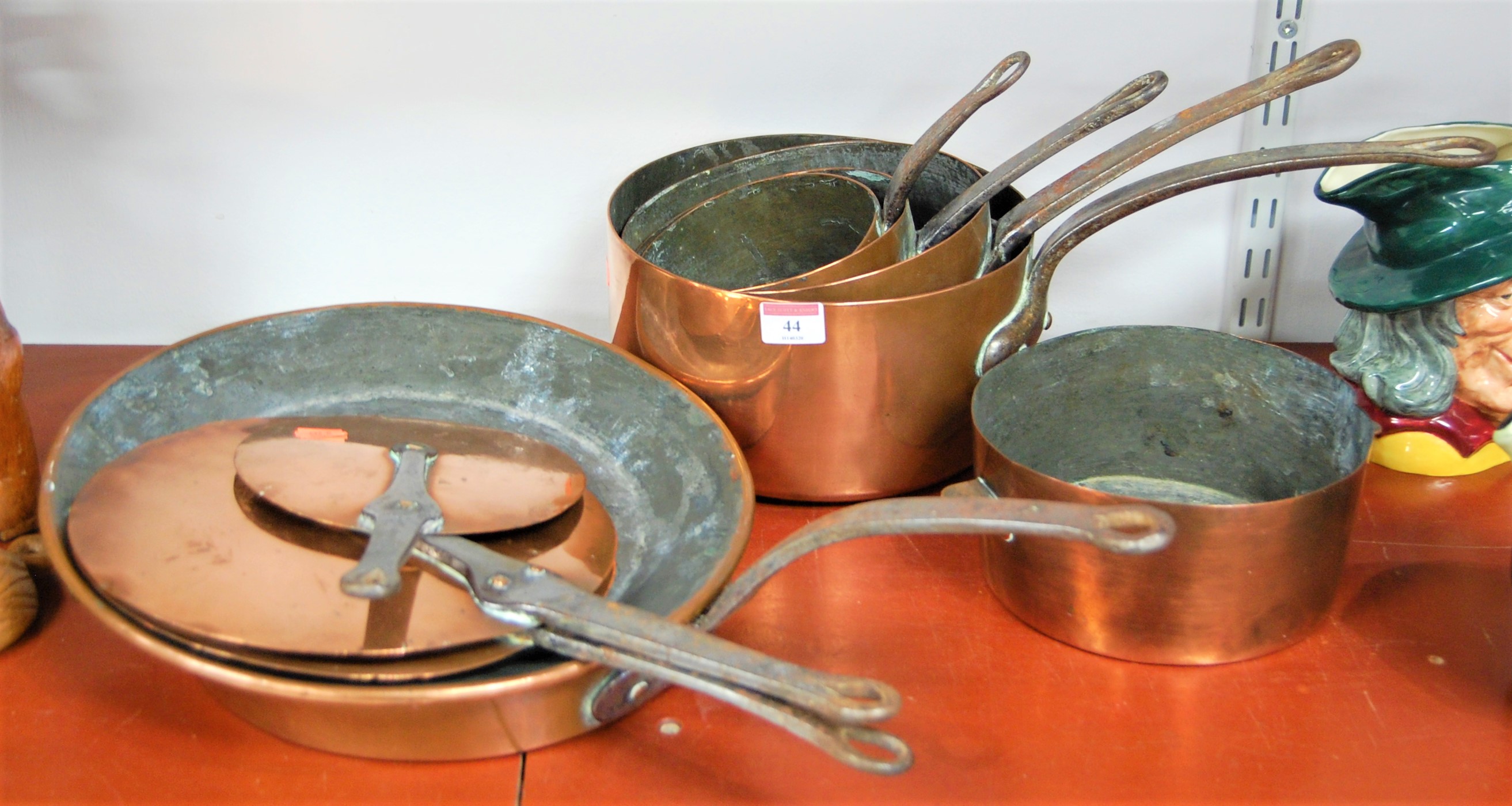 A graduated set of four copper pans each with iron handle, together with a copper saucepan, one